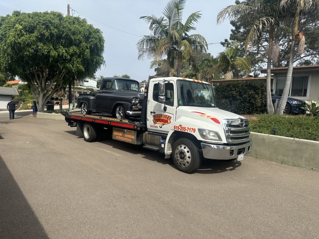 Classic car being carefully loaded onto a towing truck in San Diego.